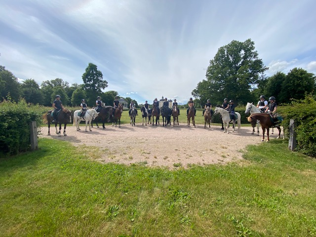 Ett tiotal ryttare med hästar står i ring i sommarfint väder.